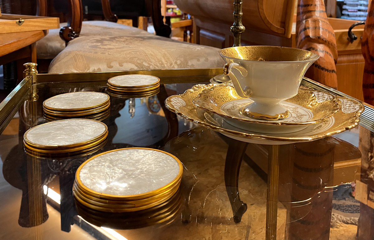 Vintage-Porzellan mit Golddekor und Perlmuttuntersetzern auf einem antiken Glastisch
